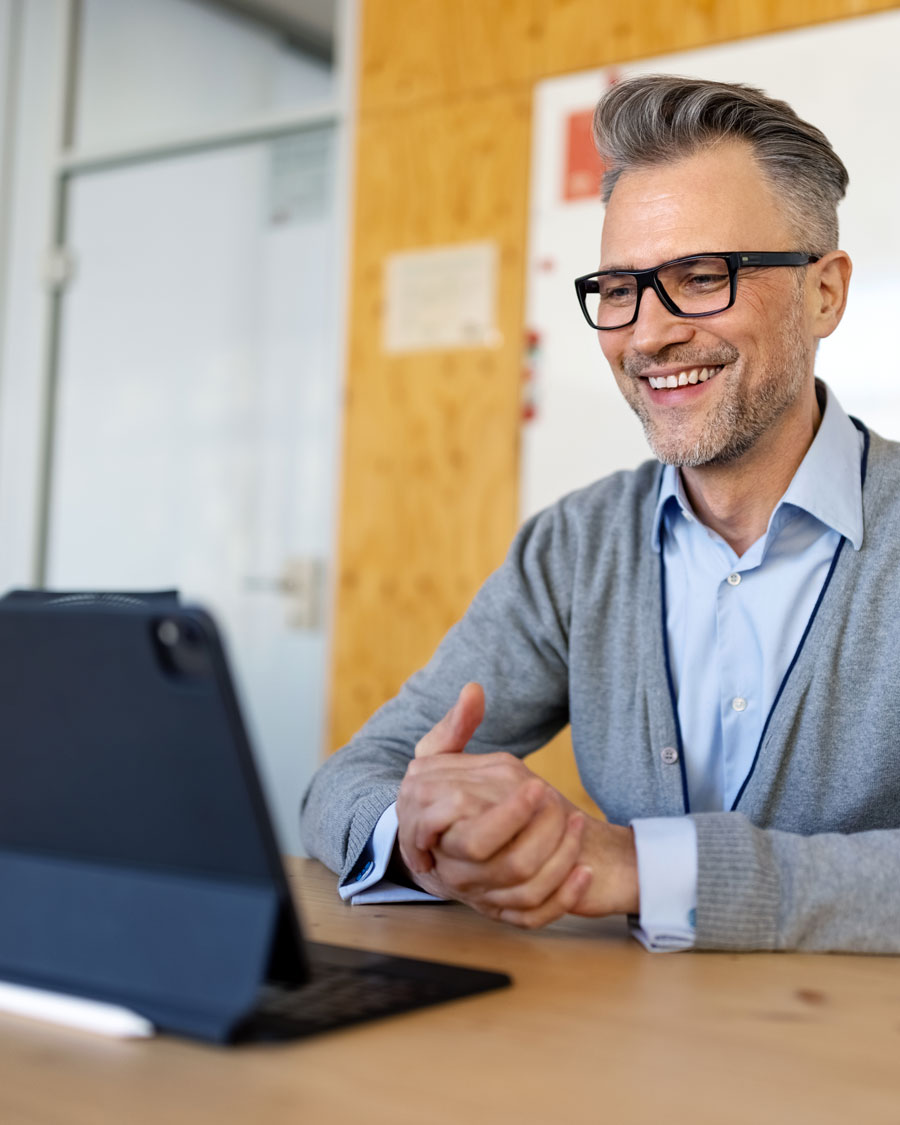 Ein Mann mit Brille und grauem Haar, lächelnd während einer Online-Beratung vor einem Tablet.