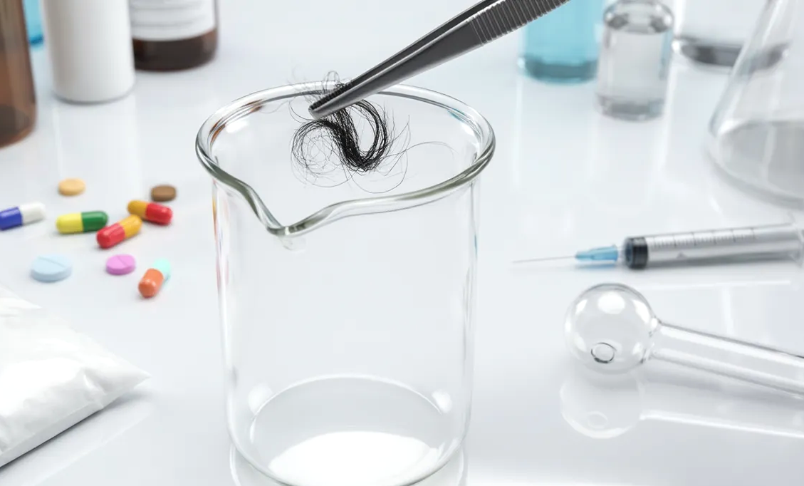 Haaranalyse im Labor: Haarprobe wird mit Pinzette in ein Glasgefäß gehalten, umgeben von Analyseutensilien.
